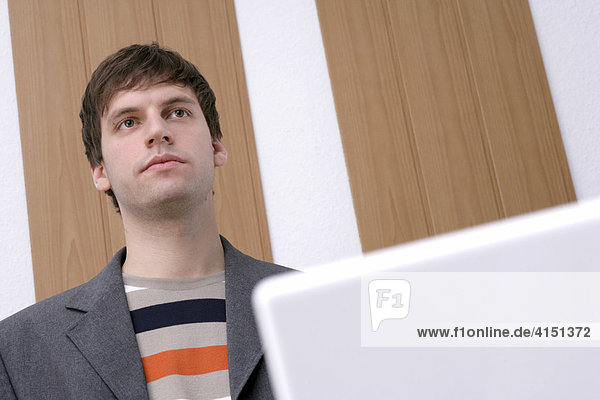 Young man standing in front of a desk  laptop in foreground