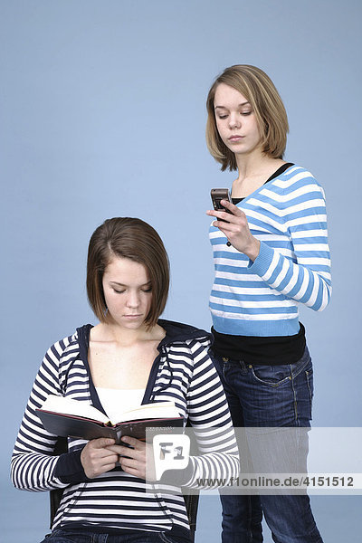 Zwei Mädchen mit unterschiedlichem Interesse  eines liest und ein anderes beschäftigt sich mit dem Handy