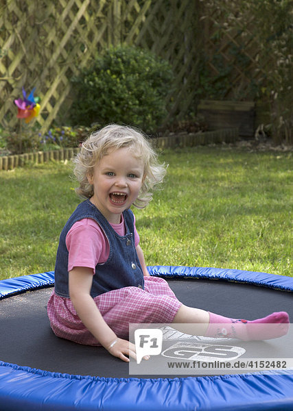 Kleines Mädchen sitzt lachend auf einem Trampolin