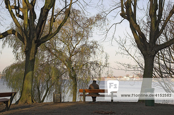 Ein Mann sitzt auf einer Bank an der Alster in Hamburg Deutschland