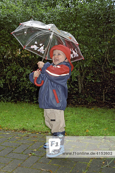 Kleines Mädchen in Regenkleidung hält einen Regenschirm und lacht Germany