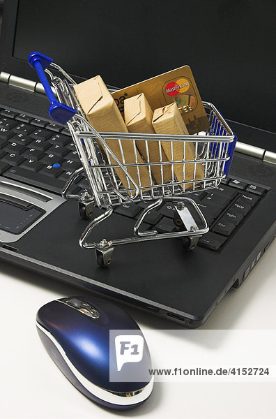 Einkaufen im Internet  ein Einkaufswagen mit Paketen und einer Kreditkarte steht auf der Tastatur eines Notebook Computers