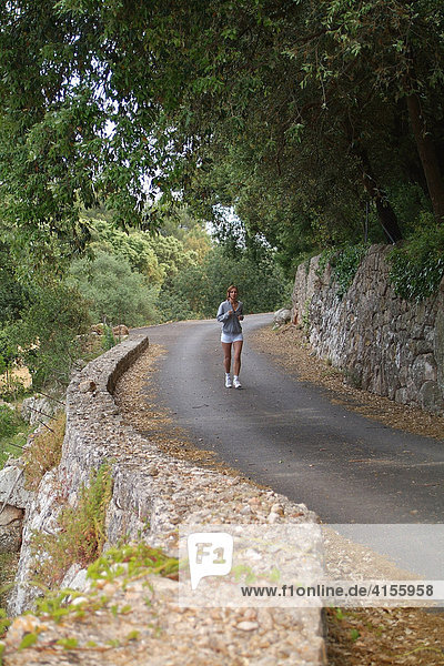 Junge Frau mit Sportkleidung beim Laufen auf einer Waldstraße