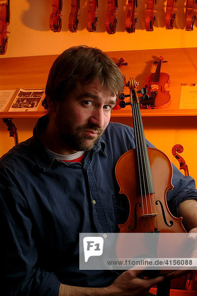 Geigenbauer mit einer Geige im Verkaufsraum