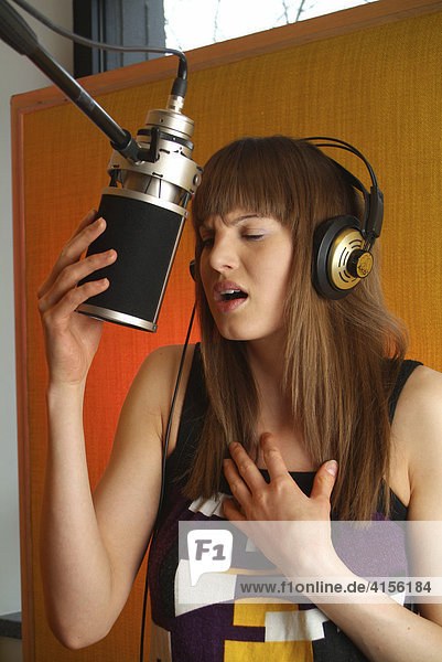 Junge Frau mit Kopfhörer singt am Mikrofon eines Tonstudios