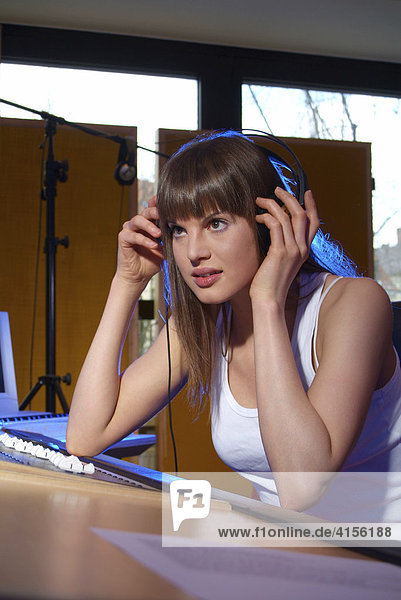 Konzentrierte junge Frau hört mit Kopfhörer am Mischpult eines Tonstudios