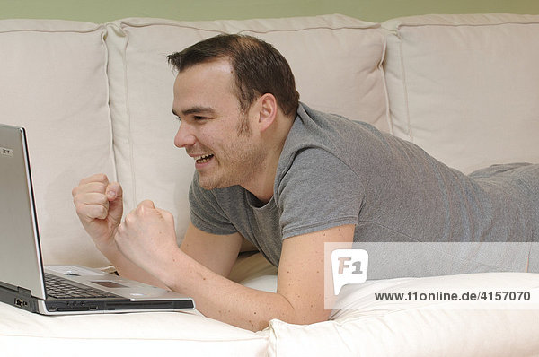 Mann auf Couch mit Laptop jubelt