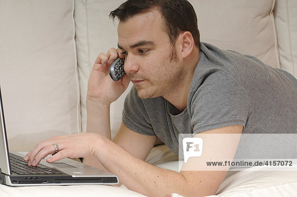 Mann auf Couch mit Laptop und Telefon
