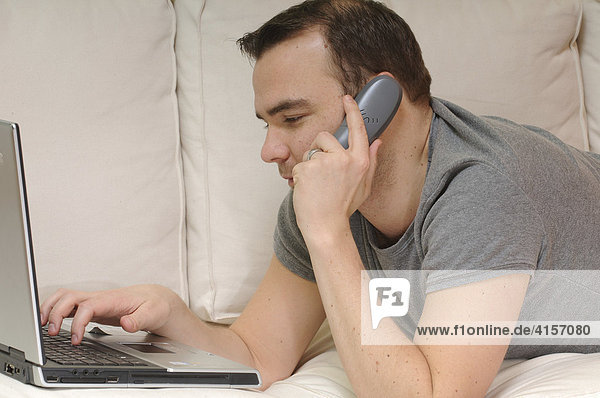 Man on a sofa with laptop and phone