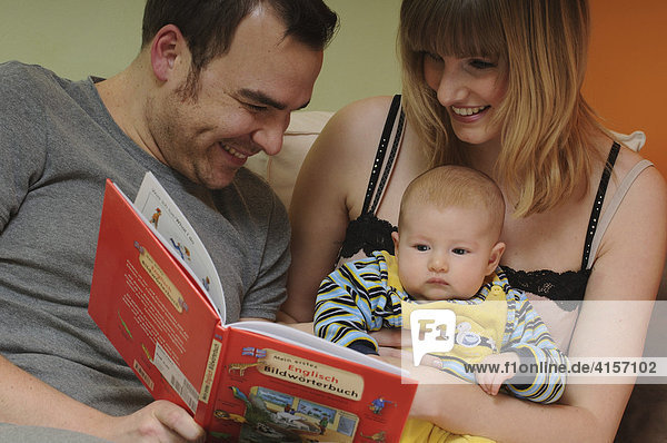 Vater  Mutter und Baby sehen sich Bildwörterbuch an