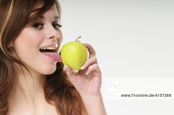 Hübsche junge braunhaarige Frau leckt an einem grünen Apfel