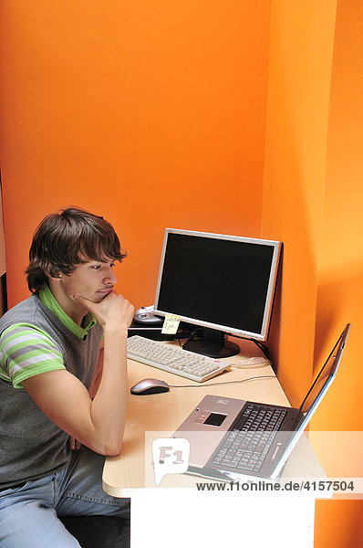 Junger Mann sitzt am Schreibtisch mit Computern