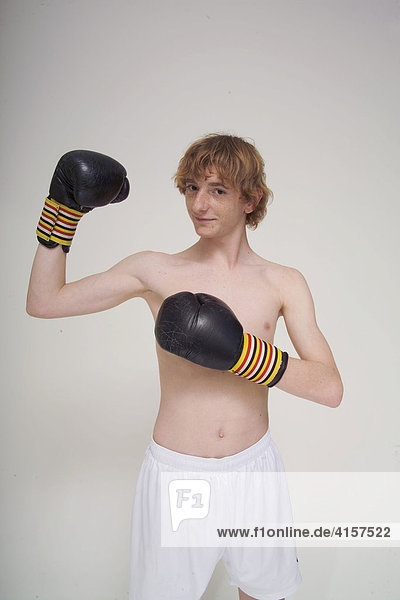 Dünner  rothaariger Junge mit Boxhandschuhen zeigt seine nicht vorhandenen Muskeln