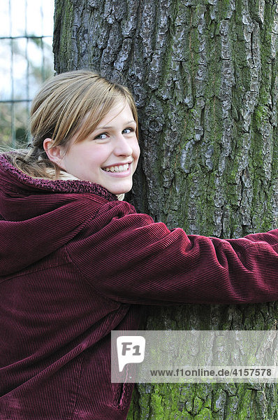 Mädchen umarmt Baumstamm im Park