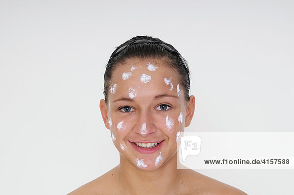 Young woman in front of a white background  dabs of lotion on her face