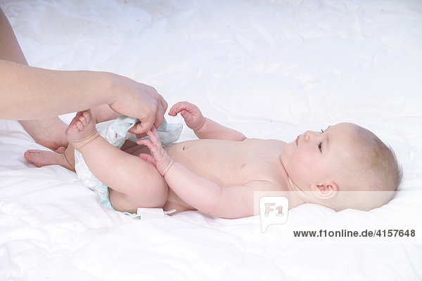 5 Monate altes Baby liegt auf weißer Decke  Windeln wechseln