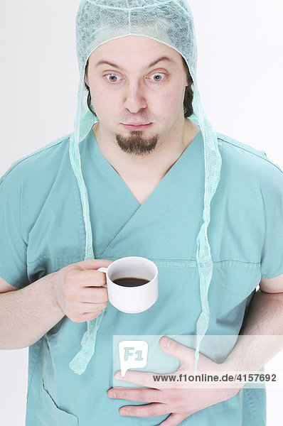Chirurg mit Tasse Kaffee fasst sich beklommen auf den Bauch
