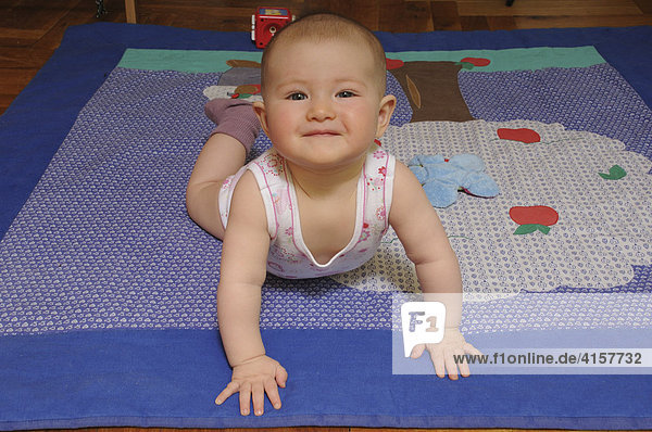 Baby in Unterhemd  Body  6 Monate  auf Spieldecke auf Boden lacht  blickt in Kamera