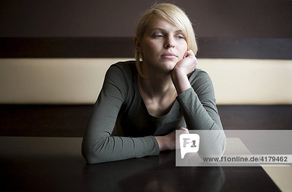 Blonde Frau sitzt traurig in einer Bar an einem Tisch