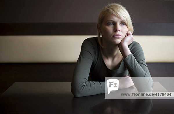 Blonde Frau sitzt traurig in einer Bar an einem Tisch