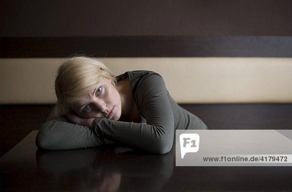 Blonde Frau liegt traurig mit dem Oberkörper auf einem Tisch in einer Bar
