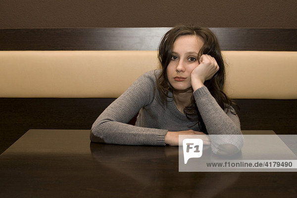 Junge Frau sitzt gelangweilt an einem Tisch in einer Bar