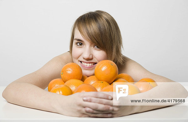 Young woman wrapping her arms around lots of oranges