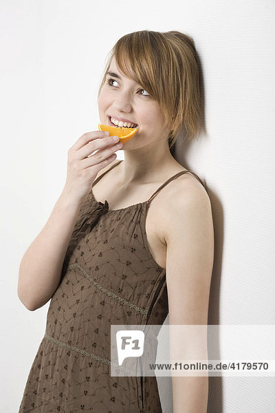 Junge Frau lehnt an einer Wand und ißt ein Stück Orange