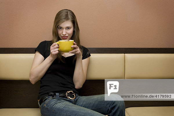 Junge Frau trinkt aus einer Tasse Milchkaffee in einer Bar