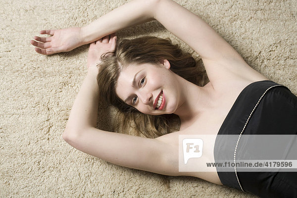 Junge Frau liegt mit schwarzem Kleid auf einem Teppich und lacht