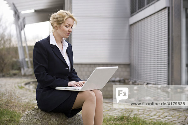 Businesswoman working on her laptop in front of an office building