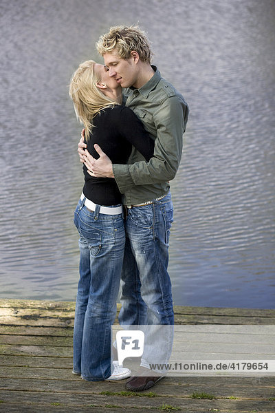 Paar umarmt und küßt sich auf einem Holzsteg am Wasser