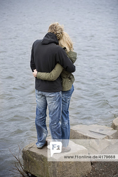 Paar umarmt sich am Wasser stehend