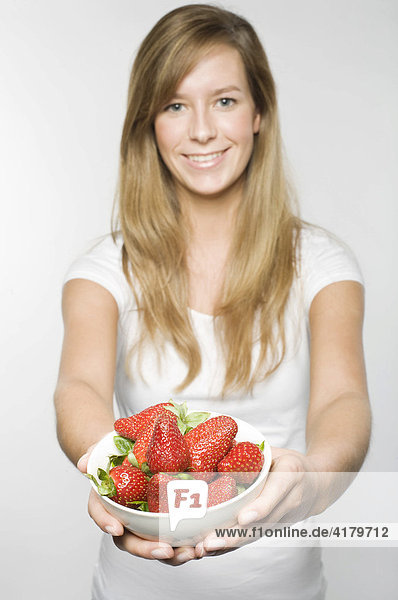Smiling young woman with long dark-blonde hair offering a bowl of fresh strawberries