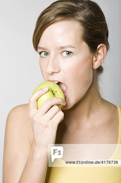 Junge Frau beißt in einen grünen Apfel