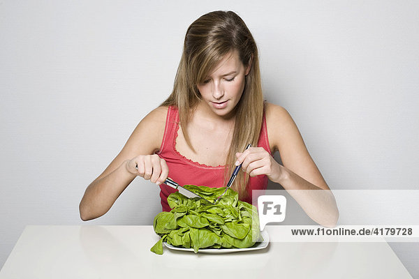 Junge Frau mit Salatkopf auf dem Teller und Besteck in der Hand