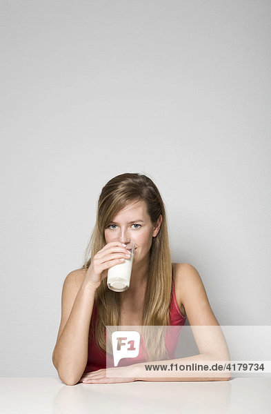 Junge Frau sitzt an einem Tisch und trinkt ein Glas Milch