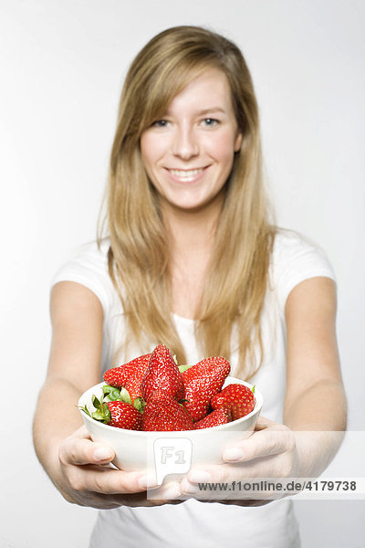 Junge Frau mit langen dunkelblonden Haaren hält lächelnd eine Schale Erdbeeren