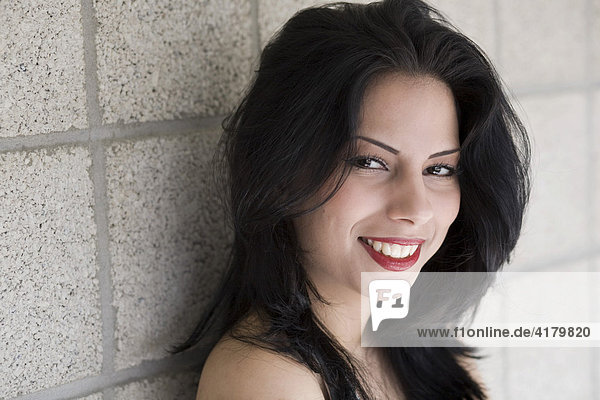 Portrait of a smiling young dark-haired woman in front of a wall