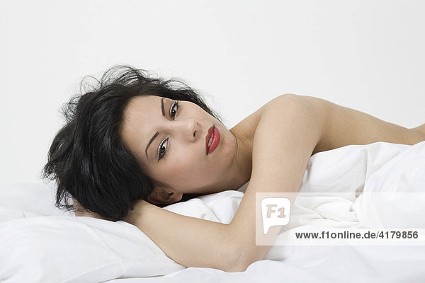 Junge  schwarzhaarige Frau liegt mit freiem Oberkörper im Bett