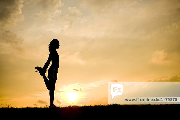 Silhouette einer Läuferin beim Stretching vor Sonnenuntergang