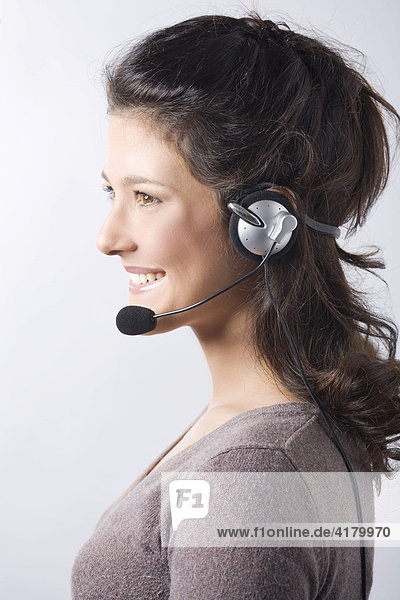 Junge dunkelhaarige Frau lacht beim Telefonieren mit Headset  Profil