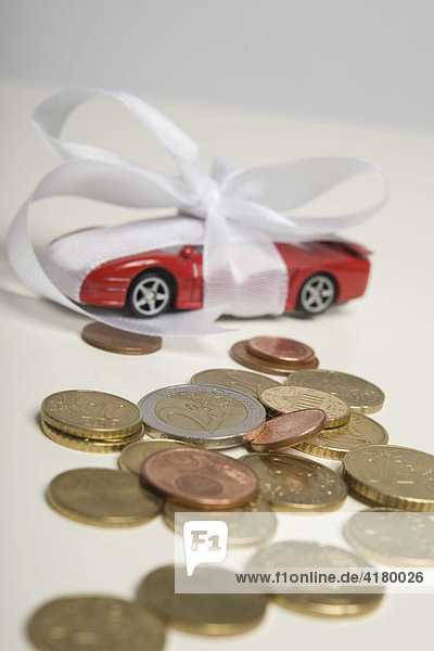 Rotes Spielzeugauto mit einer weißen Schleife als Geschenk verpackt  Euro-Münzen liegen im Vordergrund