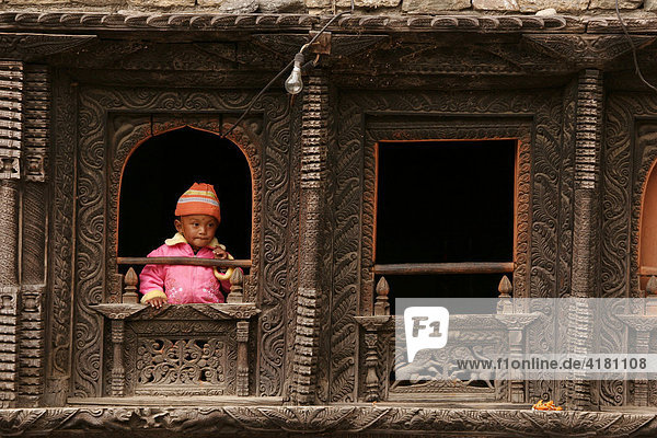 Kind sieht aus aufwändig verziertem Holzfenster im Himalaya bei Dana  Nepal  Asien Holzhaus