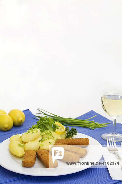 Fish sticks  tartar sauce and french fries served with a glass of white wine  lemons and chives