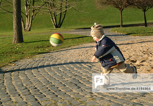 Der fast 3 jaehrige Junge auf dem gut ausgestatteten Kinderspielplatz auf dem Gelaende der Bundesgartenschau in Bonn  Rheinaue. Hier im Sandkasten einem bunten Ball nachjagen