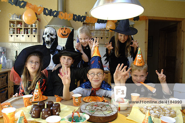 Children disguised themselves to the birthday celebration  Halloween  as ghost  witches  wizard and zombies and sit at the table with spider cakes and other creepy sweets.