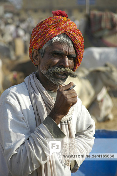 Rajput man wearing a red turban and a big moustache smoking a cigarette at a market in Karauli  Rajasthan  India