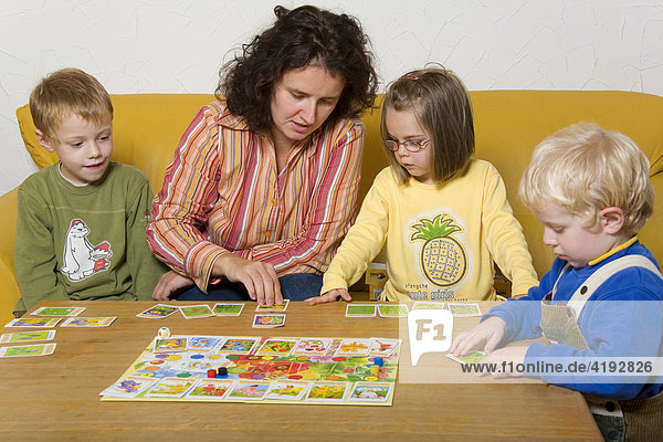Eine Erwachsene spielt mit drei Kleinkindern ein Gesellschaftsspiel