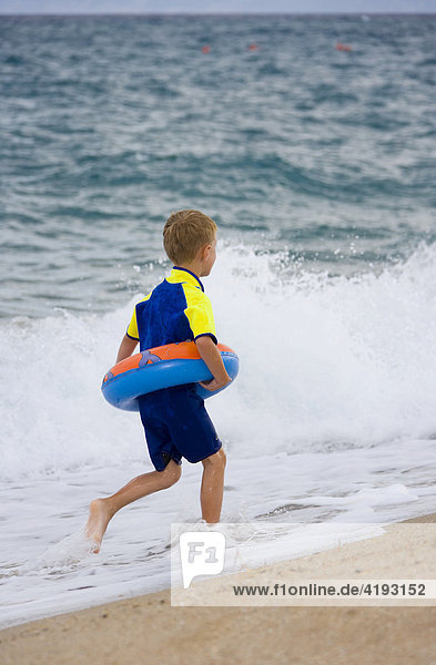 Five-year-old boy wearing flotation tire and wetsuit running along the beach in Marina di Orosei  Sardinia  Italy